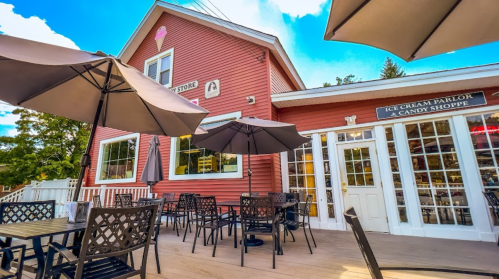 A pink ice cream parlor with outdoor seating and umbrellas, surrounded by trees and a blue sky.