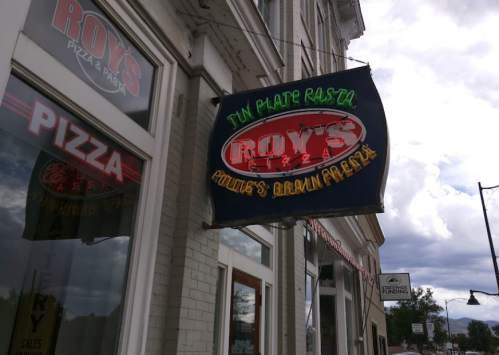 Sign for Roy's Pizza & Pasta, featuring colorful lettering against a cloudy sky.