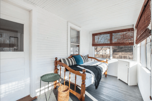 Bright sunroom with a daybed, decorative pillows, a small table, and natural light from large windows.