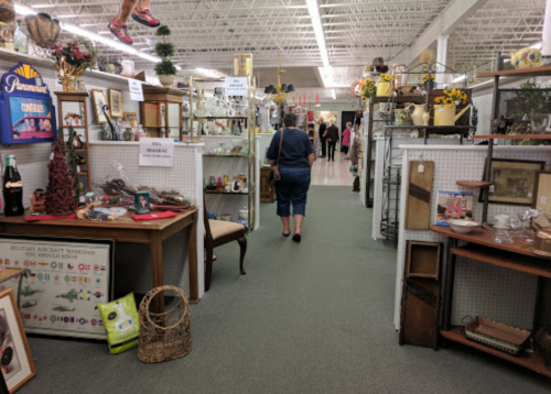 A person walks through an antique store aisle filled with various vintage items and decor on display.