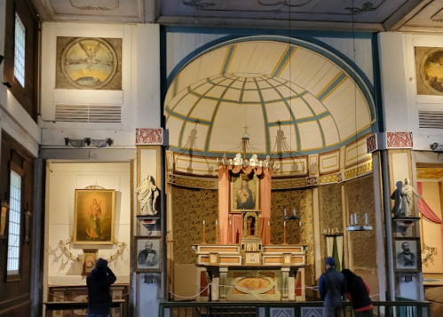 Interior of a historic chapel featuring ornate decorations, an altar, and visitors admiring the artwork.