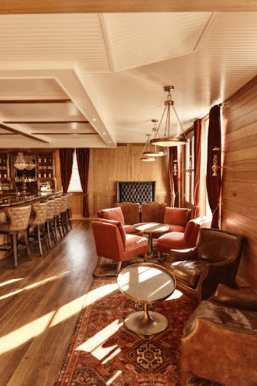 Cozy lounge with red chairs, wooden bar, and warm lighting, featuring a patterned rug and elegant decor.