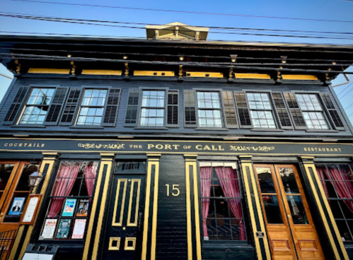 Historic black and gold restaurant facade with large windows and pink curtains, featuring the name "The Port of Call."