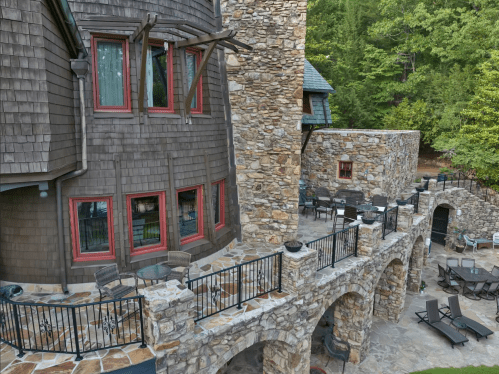 A stone and wood building with multiple levels, featuring a patio area and surrounding greenery.