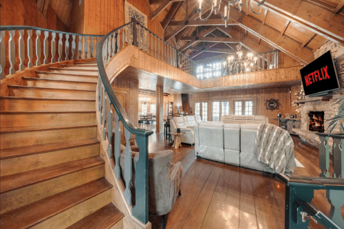 Spacious wooden interior with a staircase, cozy seating area, and a TV displaying Netflix. Warm, inviting atmosphere.