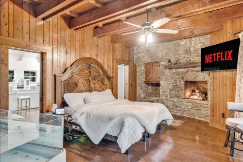 Cozy bedroom with wooden walls, a stone fireplace, and a Netflix screen on the wall.