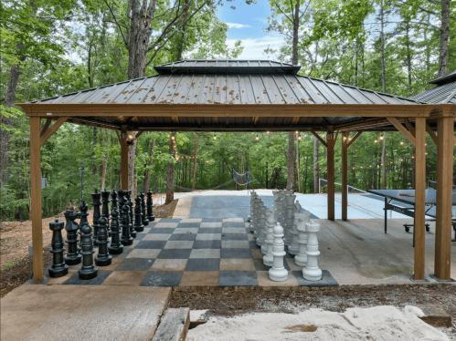Outdoor space featuring a large chess set, a ping pong table, and a serene forest backdrop.