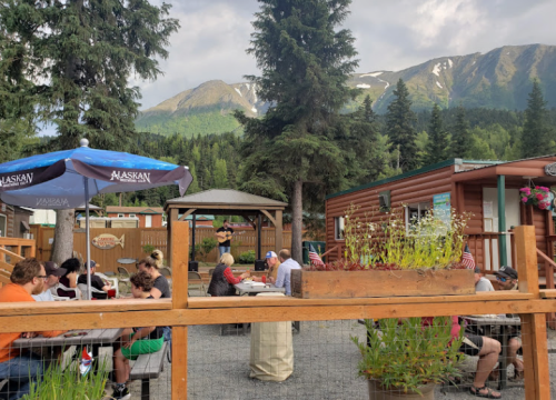 Outdoor dining area with people enjoying food, a musician performing, and mountains in the background.