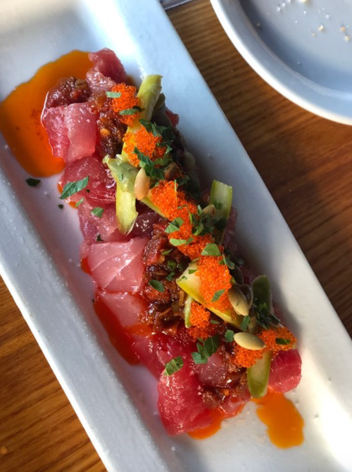 A plate of sushi featuring sliced raw fish, topped with green onions, orange roe, and a drizzle of sauce.