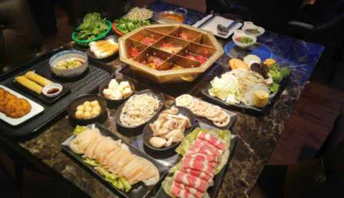 A table spread with various dishes, including sushi, vegetables, and a hot pot, arranged in an inviting layout.