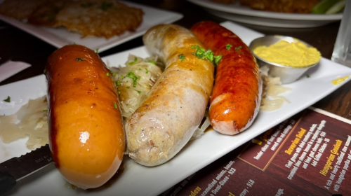 Three types of sausages on a plate with sauerkraut and a small bowl of mustard.
