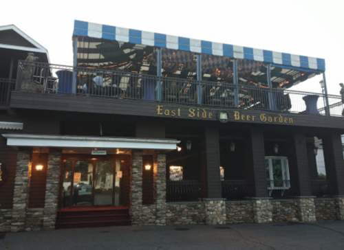 Exterior of East Side Beer Garden featuring a stone facade and a striped awning over a rooftop seating area.