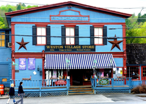 Colorful storefront of Weston Village Store with blue exterior, striped awning, and people walking by.