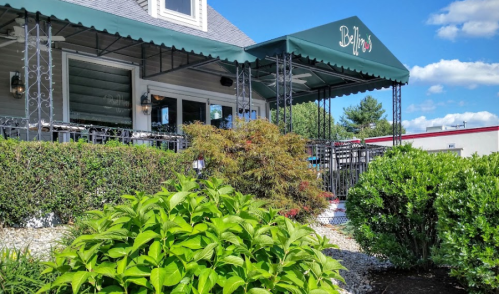 A charming restaurant exterior with a green awning, surrounded by lush greenery and a clear blue sky.