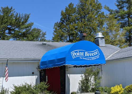 A blue awning with "Point Breeze" covers the entrance of a restaurant surrounded by trees and a clear sky.