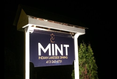 Sign for "Mint Indian Lakeside Dining" illuminated at night, featuring a phone number below the name.