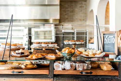 A display case filled with various baked goods, including pastries and breads, with a sign for a keto section.