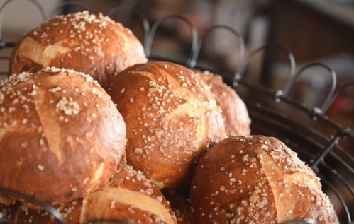 A close-up of freshly baked, golden-brown bread rolls topped with coarse salt in a wire basket.