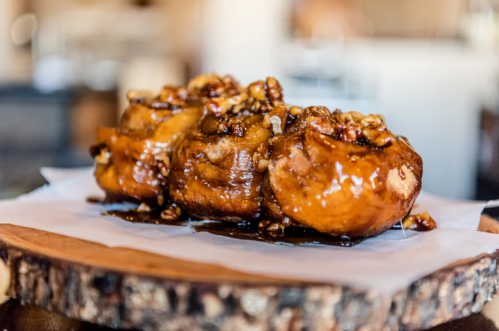 Three sticky, caramel-coated pastries topped with nuts, served on a wooden platter.
