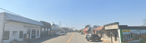 A small town street lined with shops and colorful murals under a clear blue sky.