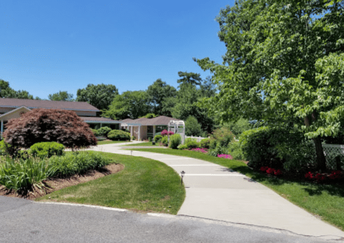A sunny pathway leads through a landscaped garden with vibrant flowers and greenery, inviting exploration.