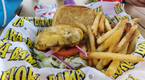 A cheeseburger with lettuce, tomato, and onion, served with a side of golden fries in a branded basket.