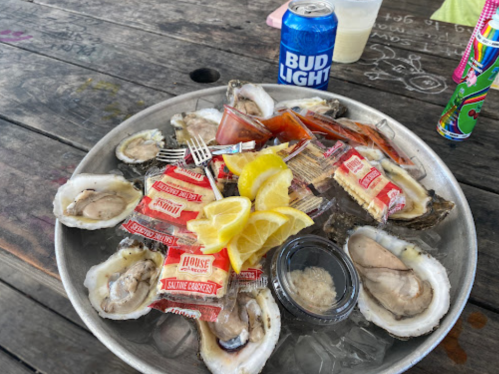A metal platter filled with oysters, lemon wedges, cocktail sauce, and saltines, alongside a can of Bud Light.