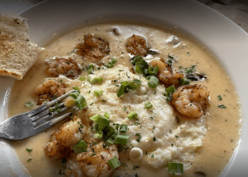 A bowl of shrimp and grits topped with green onions, served with a slice of bread on the side.