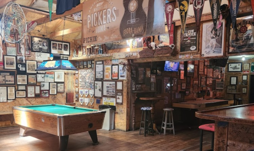 A cozy bar with a pool table, surrounded by framed photos and memorabilia on the walls, creating a nostalgic atmosphere.