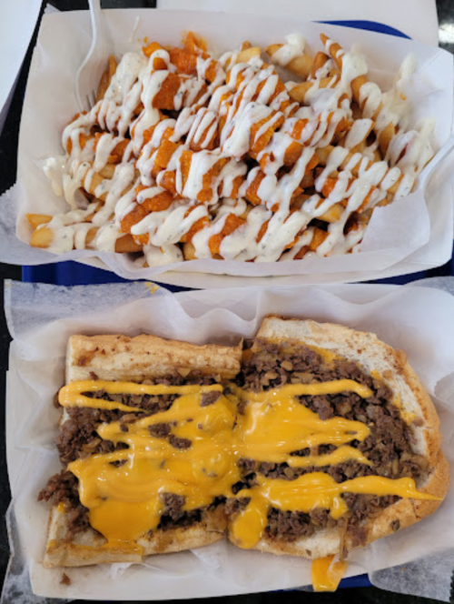 A tray with loaded fries drizzled with sauce and a cheesesteak sandwich with melted cheese on a hoagie roll.