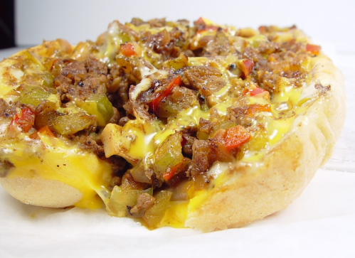 A close-up of a cheesy sandwich filled with seasoned ground beef, peppers, and onions on a toasted bun.