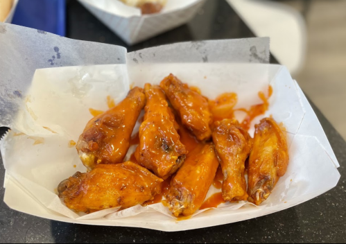 A tray of saucy chicken wings, glistening with a spicy orange sauce, served on a white paper liner.