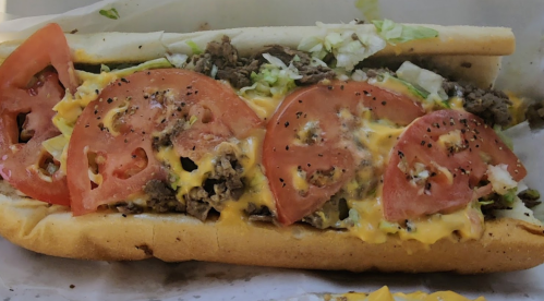 A loaded sandwich with beef, melted cheese, lettuce, and sliced tomatoes on a toasted hoagie roll.