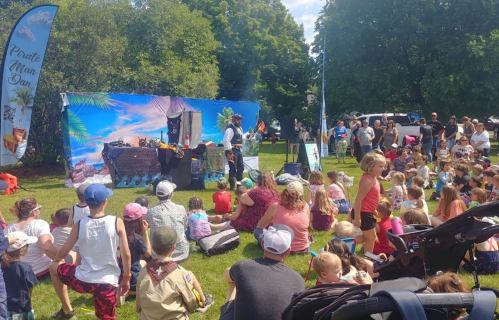 A crowd of children and families watch a performance by a pirate-themed entertainer in a park.