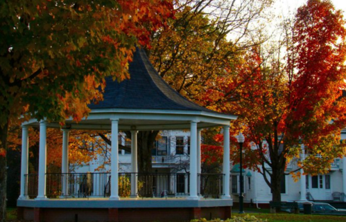 A gazebo surrounded by vibrant autumn trees with colorful leaves in a serene park setting.