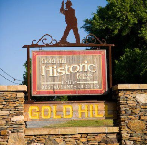 Sign for Gold Hill Historic Park & Village, featuring a miner silhouette and stone base, with shops and restaurants.