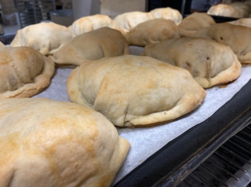 A tray of freshly baked, golden-brown calzones resting on parchment paper.