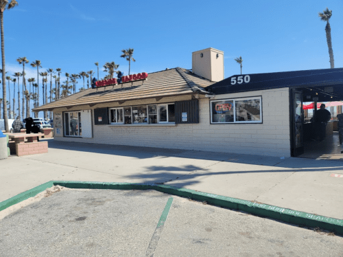 A beachside building with a sign reading "Crispy Tacos," surrounded by palm trees and a clear blue sky.