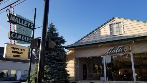 Exterior of Malley's Candies with a sign wishing "Happy 4th Birthday Addie" and a clear blue sky in the background.