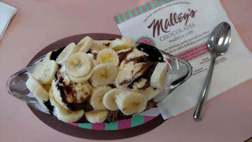 A dessert bowl filled with ice cream, chocolate sauce, and sliced bananas, next to a napkin from Malley's Chocolates.