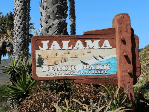 Sign for Jalama Beach Park in Santa Barbara County, featuring palm trees and a coastal scene.