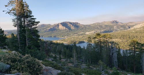A scenic view of a lake surrounded by mountains and dense pine trees under a clear sky.