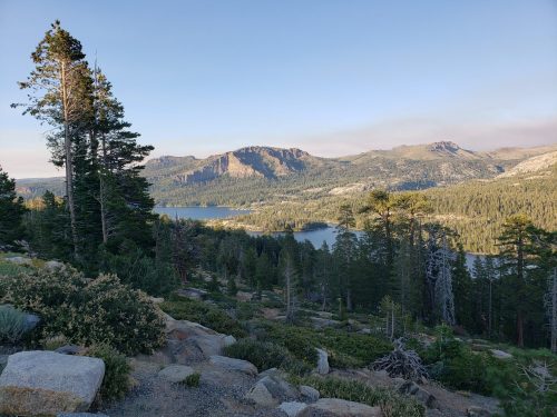 A scenic view of a lake surrounded by mountains and trees under a clear sky.