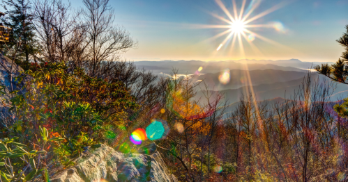 A scenic mountain view at sunrise, with vibrant colors and lens flare effects illuminating the landscape.