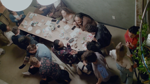 A group of people gathered around a long table, enjoying food and drinks in a cozy, well-lit setting.