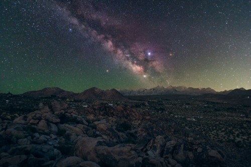 A stunning night sky filled with stars and the Milky Way over rocky terrain and distant mountains.