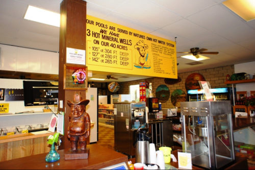Interior of a cozy café featuring a wooden statue, colorful decor, and a sign about hot mineral wells.