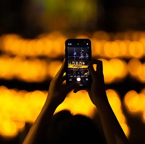 A person holds a smartphone, capturing a vibrant display of lights in a blurred, glowing background.