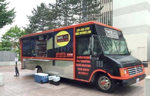 A food truck parked in an urban area, featuring a colorful design and menu displayed on the side.