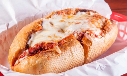 A cheesy stuffed bread bowl filled with marinara sauce and meat, resting in a red basket lined with white paper.